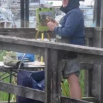Artist painting outside at a dock